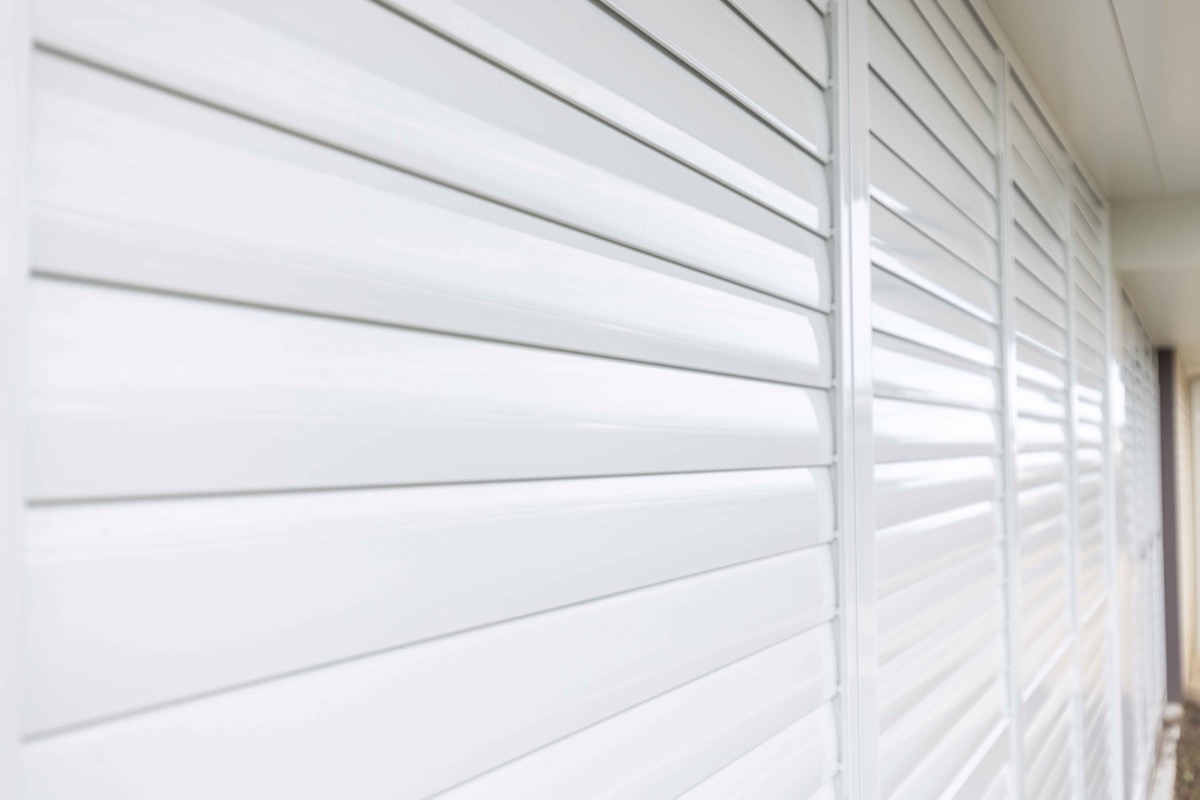 Angled view along a closed wall of white aluminium shutters inside a patio enclosure