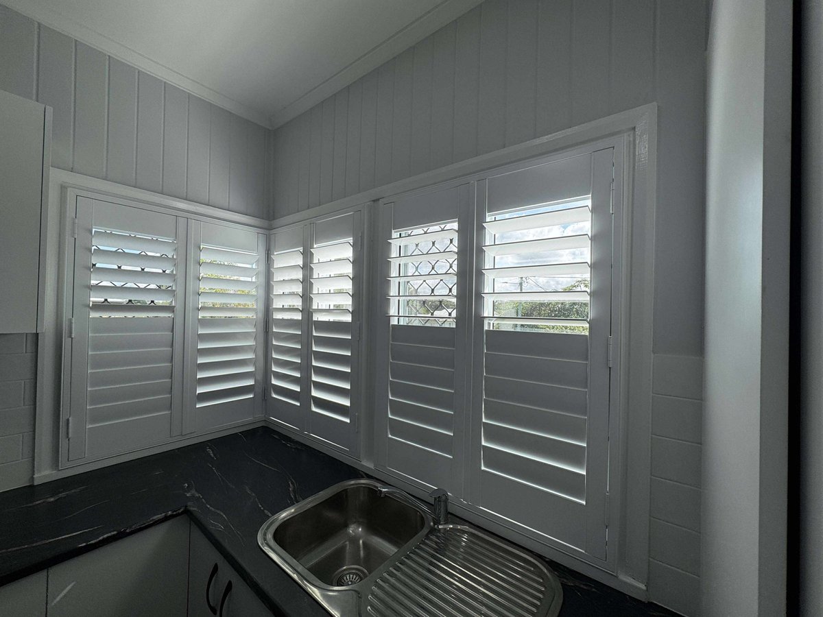White plantation shutters on the corner windows over a kitchen sink
